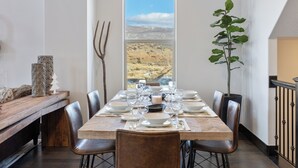 Un comedor con una mesa dispuesta para seis personas, vista al paisaje a través de una ventana y una planta a la derecha.