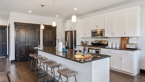 Cocina moderna con armarios blancos, una isla grande con taburetes de bar, electrodomésticos de acero inoxidable e iluminación colgante.
