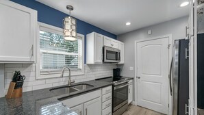 Una cocina moderna con armarios blancos, encimera de granito, refrigerador de acero inoxidable y horno empotrado.