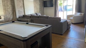 Een moderne woonkamer met een pooltafel, een zithoek en een flatscreen televisie aan de muur.