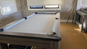 Een pooltafel met houten frame, een bakstenen muur en een raam met jaloezieën.