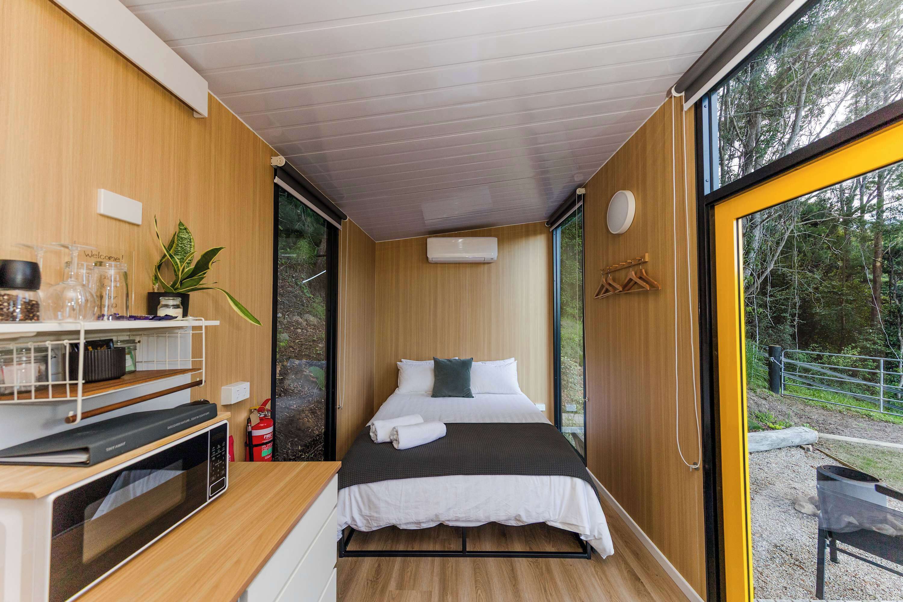 A compact bedroom with a bed, bedside table, and a view of the outdoors.