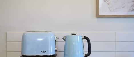 Eine Küchenarbeitsplatte mit einem Toaster und einem Wasserkocher, ein gerahmtes Bild an der Wand und ein Stapel Bücher.