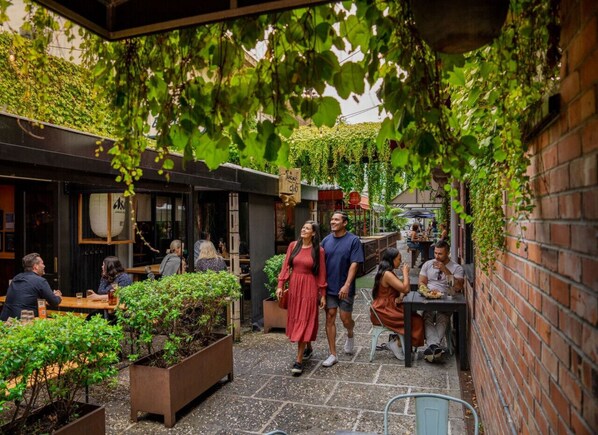Un café en plein air, avec des tables et des chaises, entouré de verdure et de murs en briques.