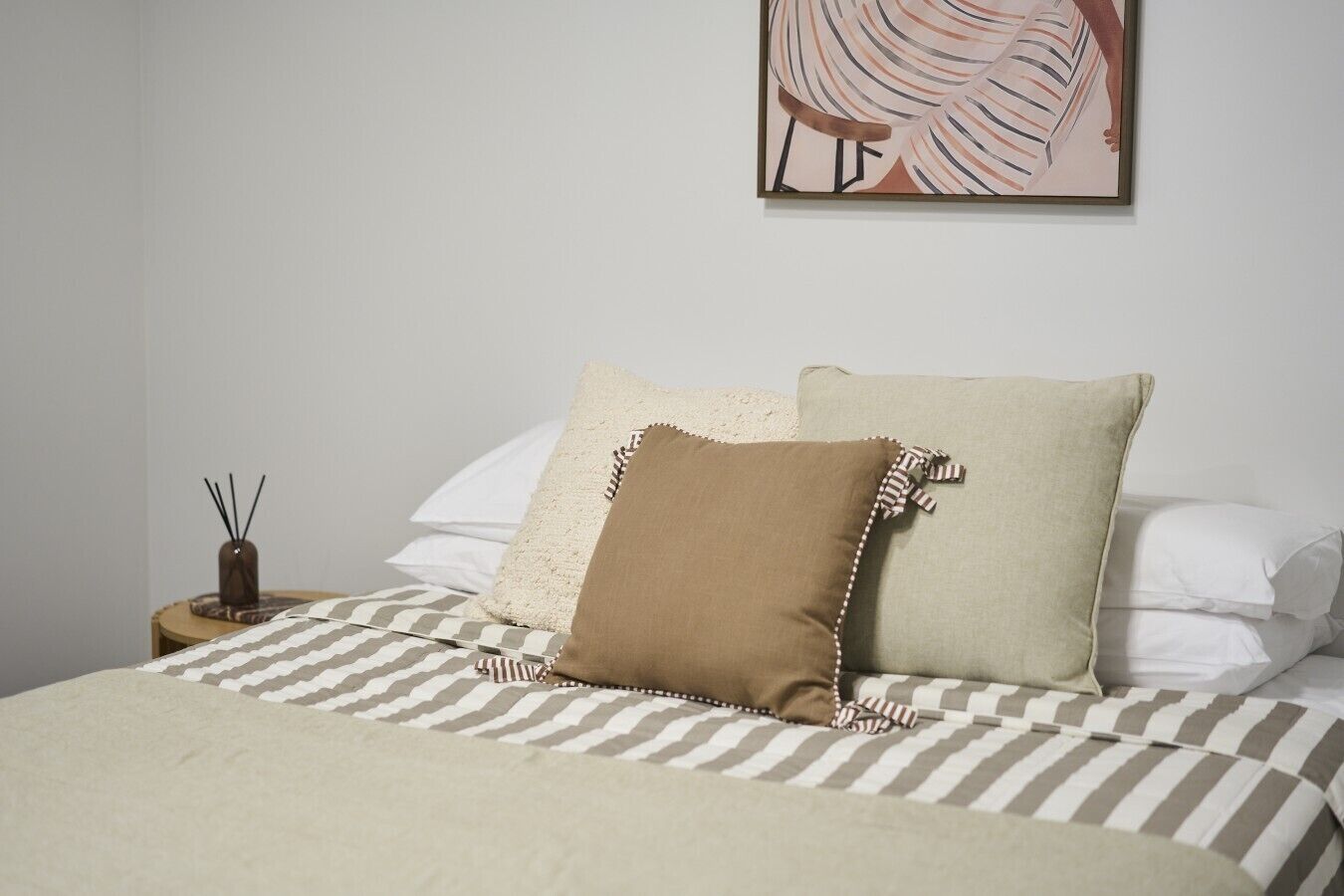 A neatly made bed with striped bedding and two pillows, a small bedside table with a candle, and a wall art piece.