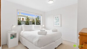 A modern bedroom with a large bed, a bedside table with a lamp, a window with a view of buildings, and a framed artwork on the wall. - Cosy St Marys Bay Retreat with Parking (Auckland)