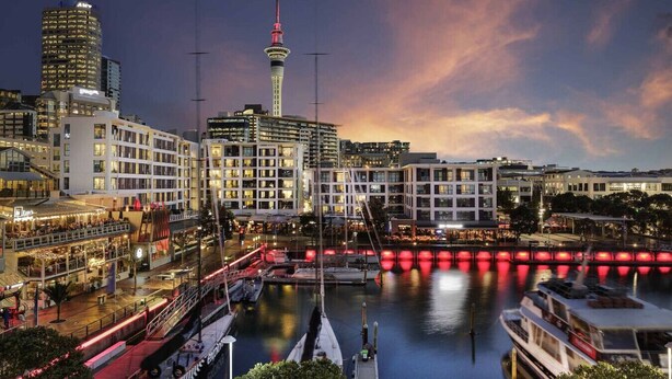 A waterfront cityscape with modern buildings, a prominent tower, and a marina with boats. - Cosy Studio in the Award-Winning Union & Co (Auckland)