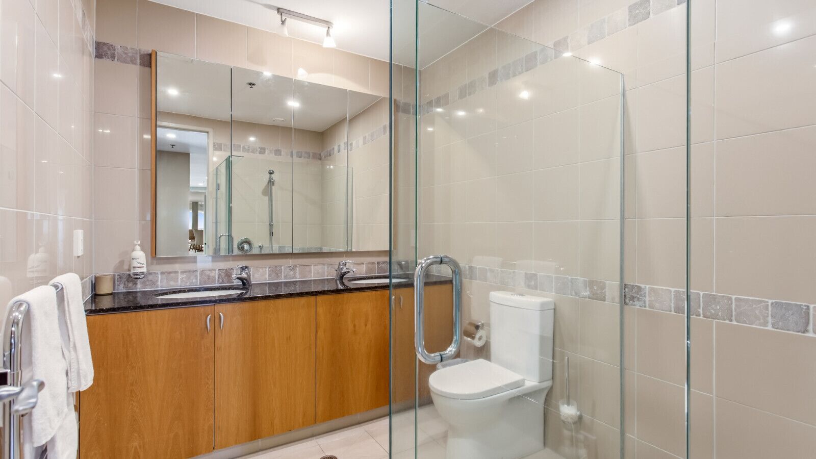 Een moderne badkamer met een douchecabine van glas, een houten wastafelmeubel en een wit toilet.