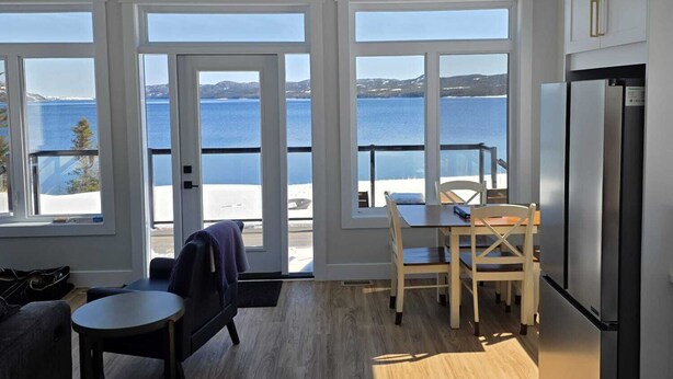 Cozinha moderna com grandes janelas, área de refeições e vista para o mar.
