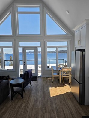 A modern kitchen with large windows, a dining area, and a view of the sea. - Cozy Beachfront Cottage Retreat w/ Loft Workspace, Stunning Views & Beach Access (King's Point)