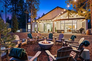 A modern house with a fire pit, outdoor seating, and string lights.