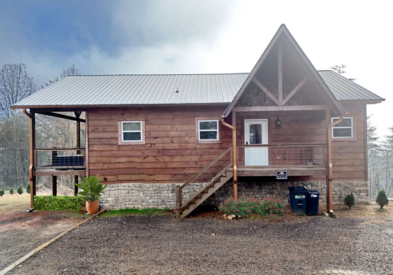 Une cabane en bois avec un toit en métal, une véranda et un escalier menant à l’entrée.