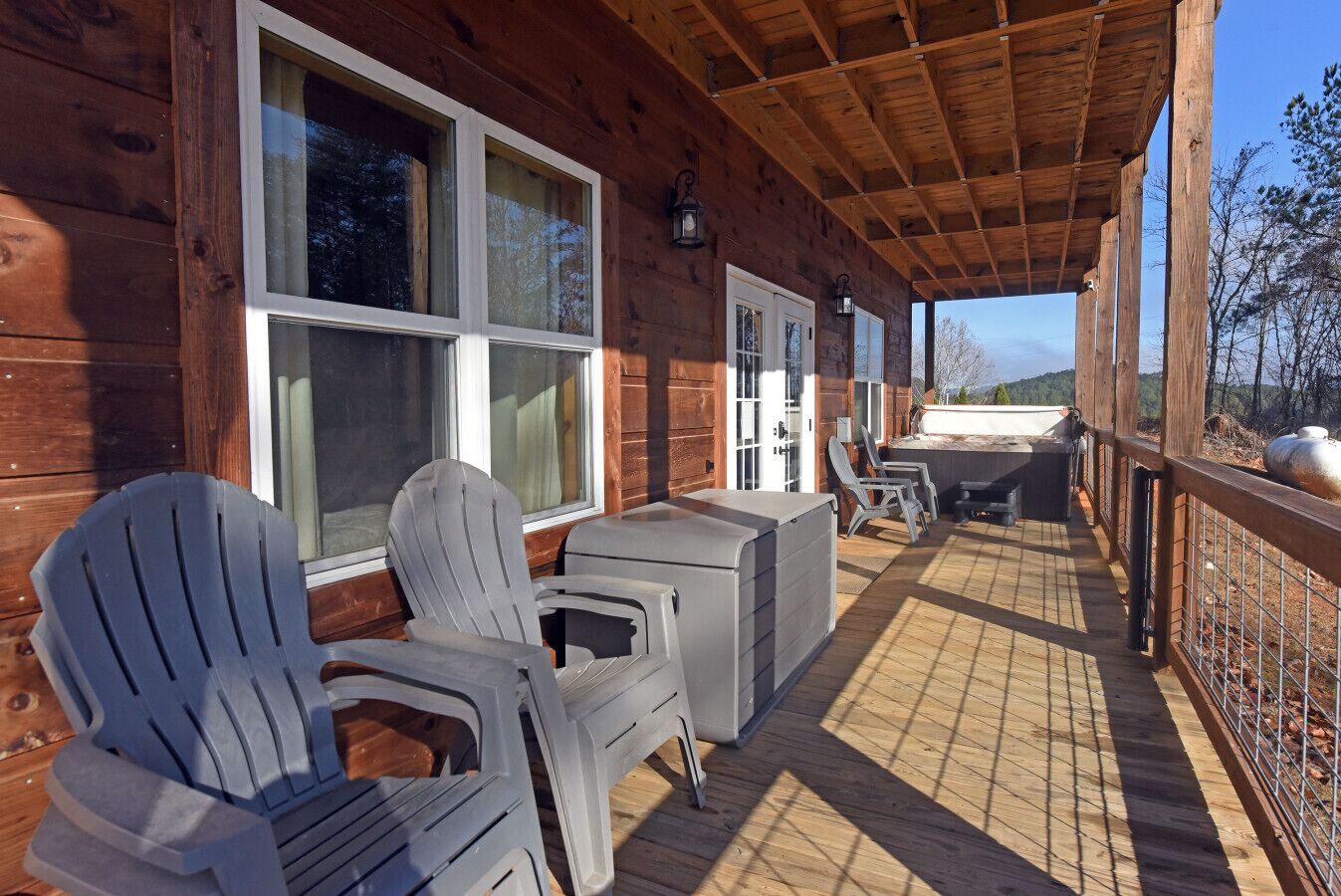Eine Holzhütte mit überdachter Veranda, Sitzgelegenheiten im Freien und großen Fenstern.