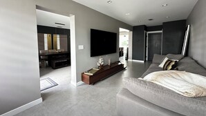 A modern living room with a grey sofa, a flat-screen TV, and a wooden entertainment unit. - Casa Solea Miami • Pool Home w/ Workspaces + Master Office & Daybed (Miami)