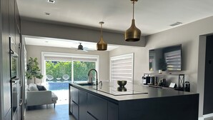 A modern kitchen with a large central island, a ceiling fan, and a large window overlooking a garden. - Casa Solea Miami • Pool Home w/ Workspaces + Master Office & Daybed (Miami)