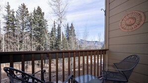 A wooden deck with metal chairs and a table, overlooking a forest and mountains. - Charming 1-bedroom condo at Cascade Village with stunning mountain views - 2 Miles from Purgatory (Durango)