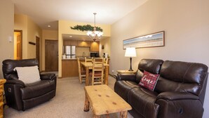 A living room with a brown leather sofa, a wooden coffee table, and two leather armchairs. There is a dining area in the background with a wooden table and chairs. - Charming 1-bedroom condo at Cascade Village with stunning mountain views - 2 Miles from Purgatory (Durango)