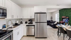 Uma cozinha moderna com armários brancos, uma geladeira de aço inoxidável, uma cafeteira e uma área de jantar com mesa e cadeiras.