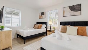 Quarto de hotel com duas camas, uma mesa de cabeceira, luminária e obras de arte nas paredes.