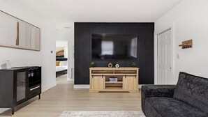 Uma sala de estar moderna com uma TV de tela plana, um sofá escuro, um móvel de entretenimento em madeira e um armário preto.