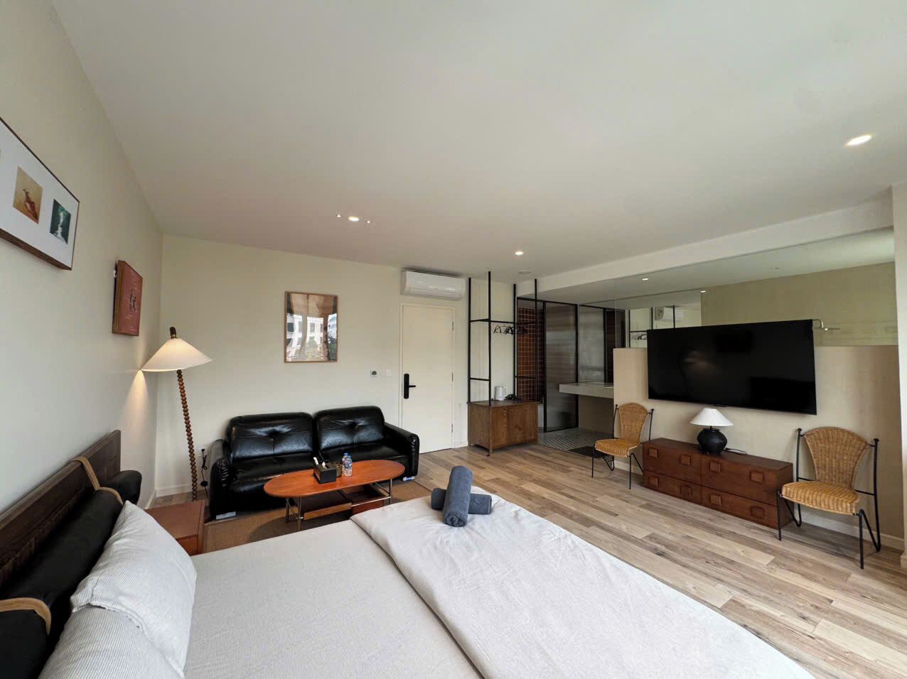 Una moderna camera d'albergo con un letto grande, un divano in pelle nera, un tavolino di legno, una TV e un piccolo angolo relax con poltrone in vimini.