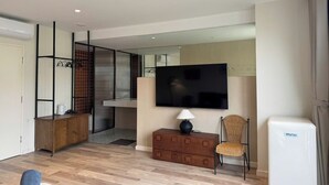 A modern living room with a flat-screen TV, a wooden cabinet, a wicker chair, and a mini fridge. - Calmstay-Soluna Pearl Villa-Ocean Park (Nghia Tru)