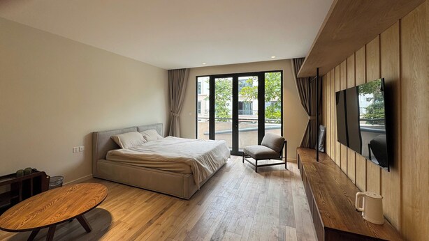 A modern bedroom with a bed, a chair, a table, and a TV mounted on the wall. - Calmstay-Soluna Pearl Villa-Ocean Park (Nghia Tru)