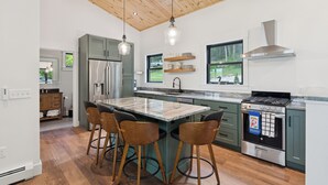 Una cucina moderna con isola centrale, sgabelli da bar, frigorifero in acciaio inossidabile e piano cottura a gas.