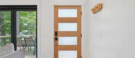A modern interior with a wooden door, a glass door leading to an outdoor area, and a white wall with a wooden art piece.