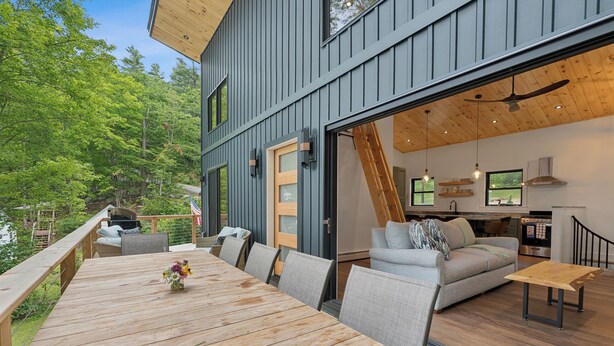 Una casa moderna con una terrazza, un'area pranzo con tavolo in legno e un soggiorno con divano e televisione.