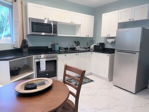 A modern kitchen with white cabinets, a stainless steel refrigerator, a microwave, and a stove. - THE COTTAGE: Cozy Studio, Steps Away From Grace Bay Beach and Grace Bay Strip! (Grace Bay)
