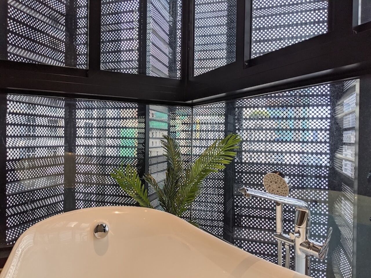 A modern bathroom with a freestanding bathtub, a shower area, and a large window with a metal mesh design.