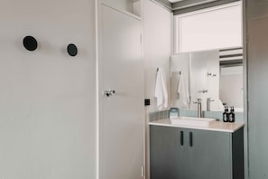 A bathroom with a white door, a mirror, a sink, and two black circular objects on the wall. - The Black Dolphin Motel and Holiday Park (Merimbula)