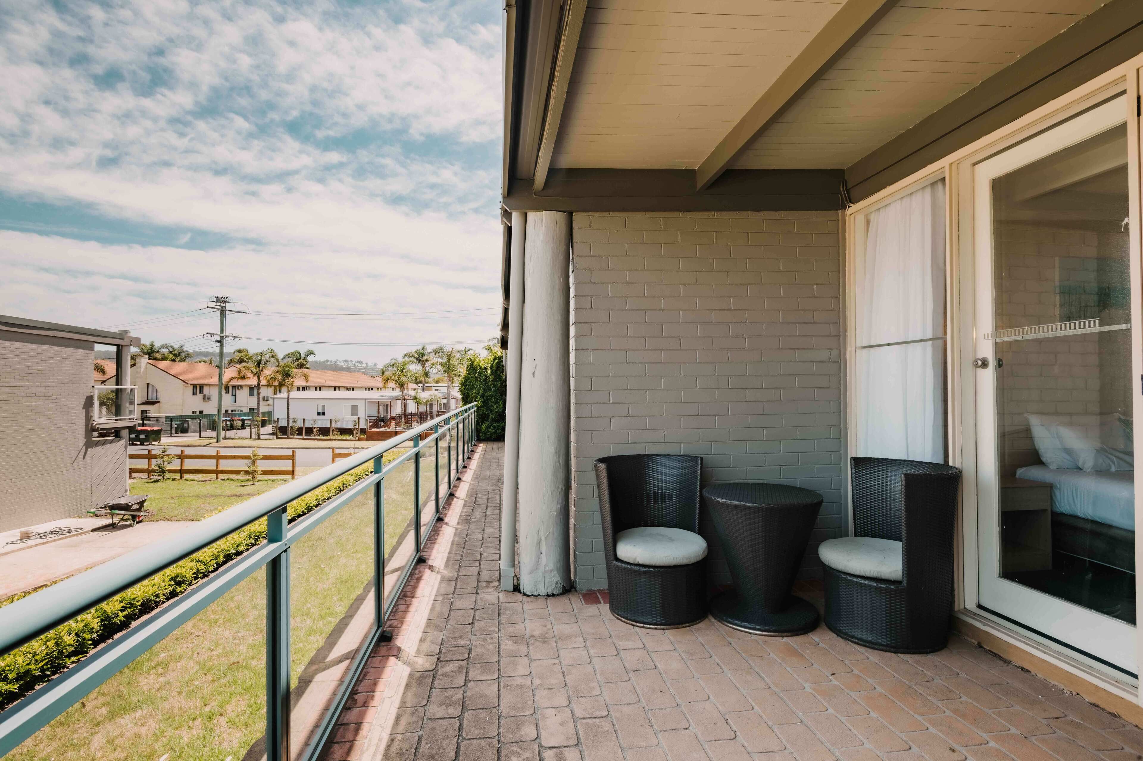 A balcony with wicker chairs, a glass door, and a view of a residential area.