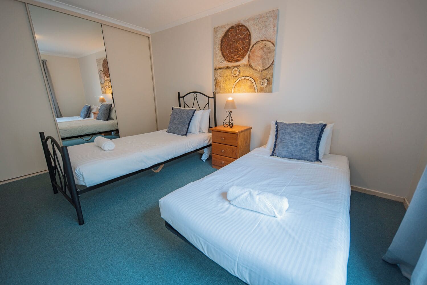 Een hotelkamer met twee bedden, een kaptafel, een spiegel en een kunstwerk aan de muur.