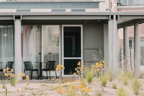 An outdoor seating area with chairs and tables, a covered entrance, and yellow flowers in the foreground. - The Black Dolphin Motel and Holiday Park (Merimbula)