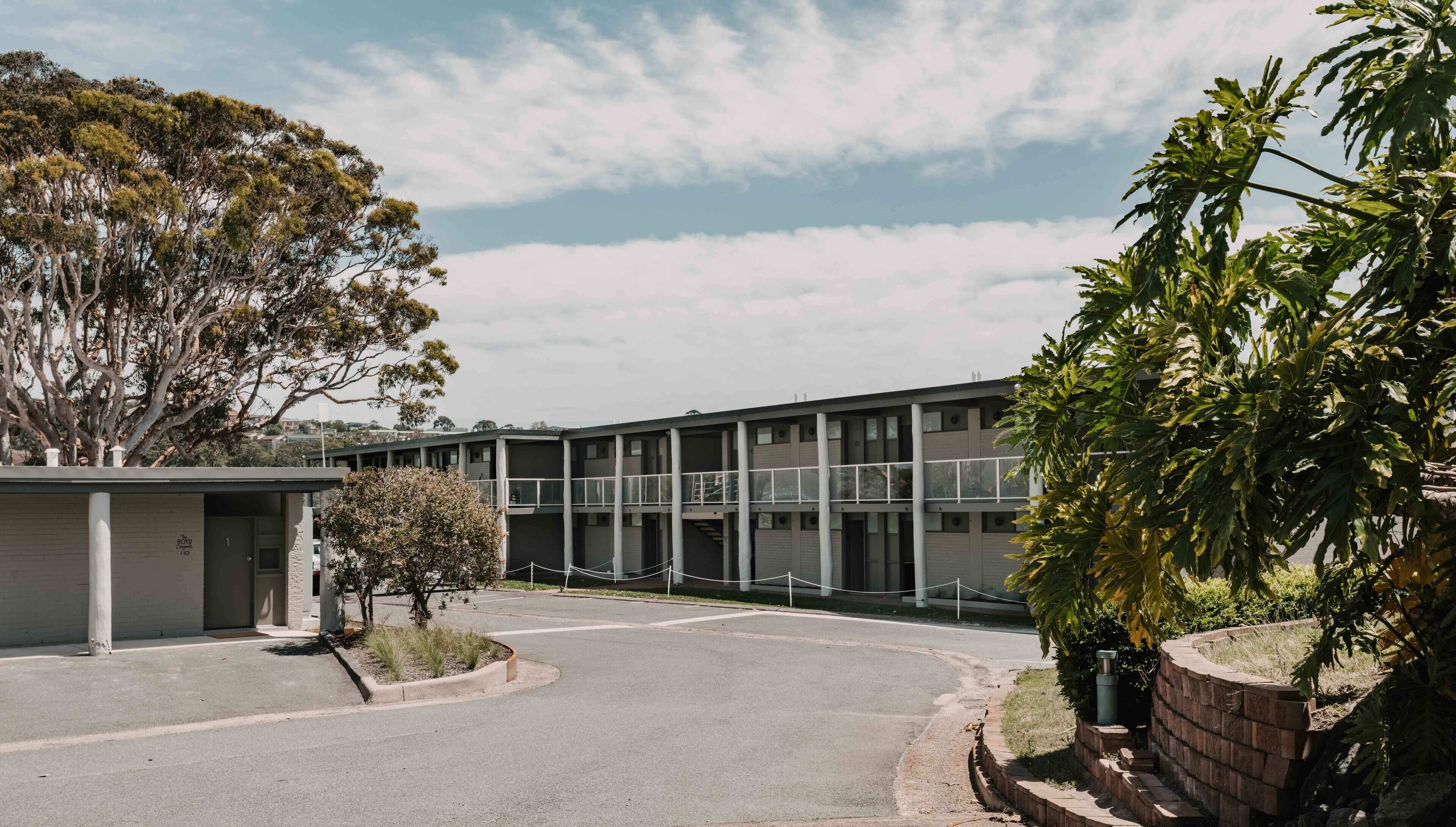 A modern building with a flat roof, large windows, and a parking area.