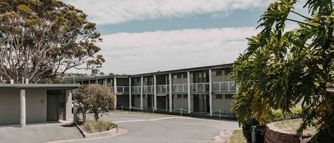 A modern building with a flat roof, large windows, and a parking area.