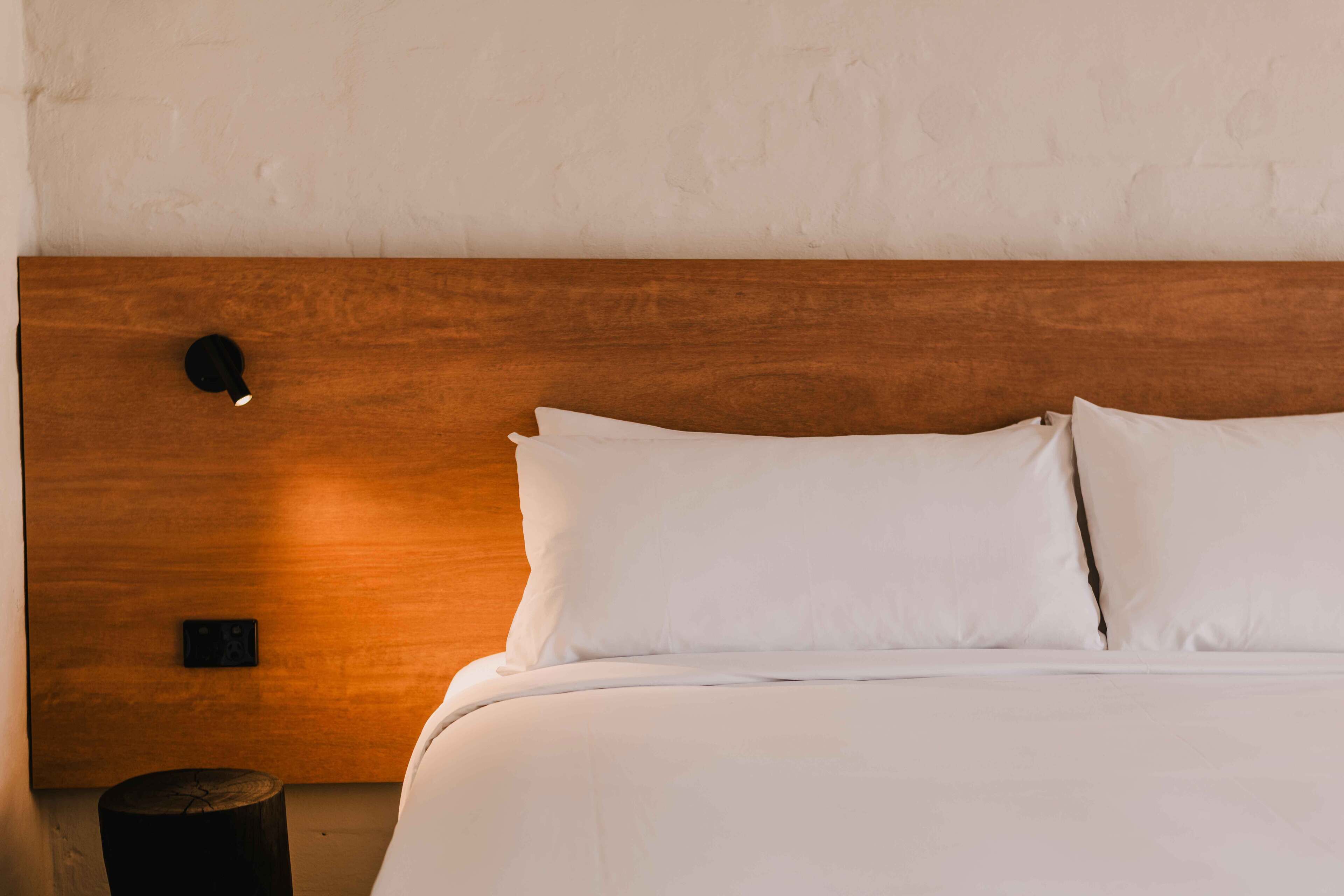 A neatly made bed with white linens and a wooden headboard.