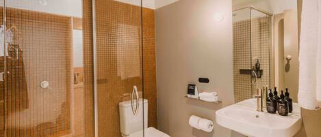 A bathroom with a glass shower enclosure, a toilet, a sink with toiletries, and a mirror.