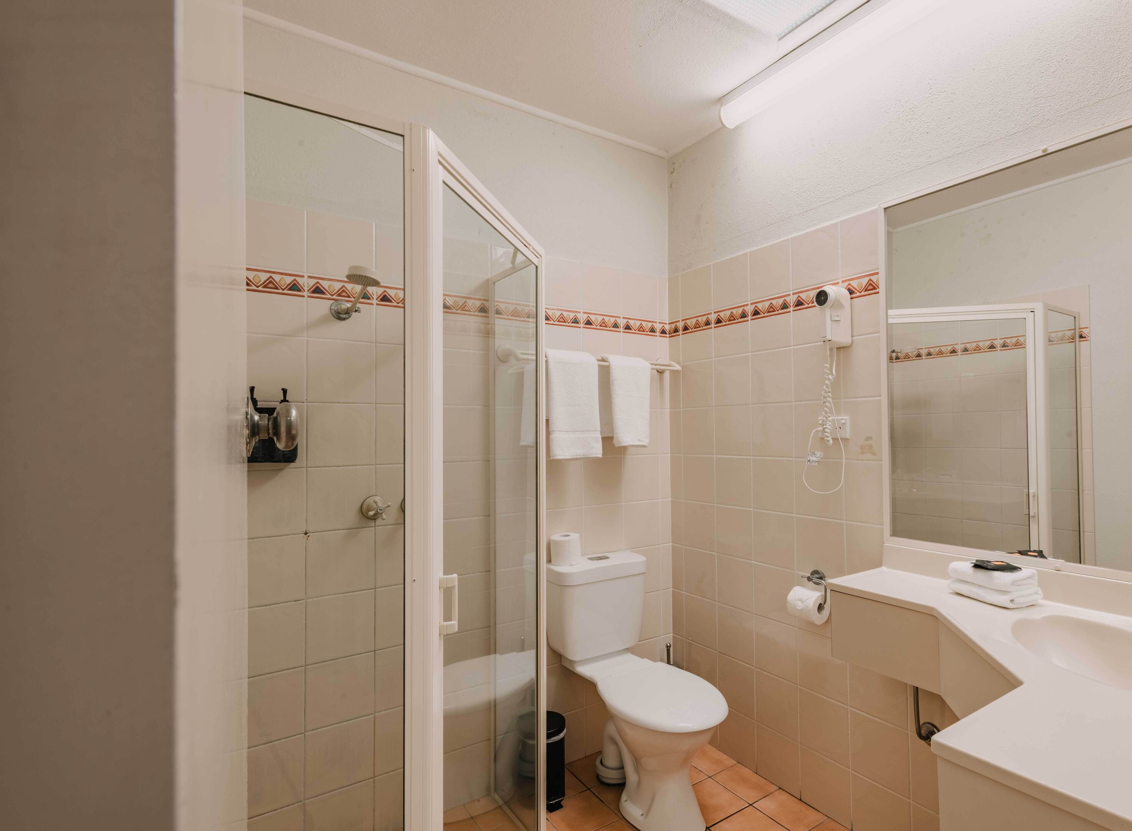 A bathroom with a glass-enclosed shower, a toilet, a sink, and a mirror.