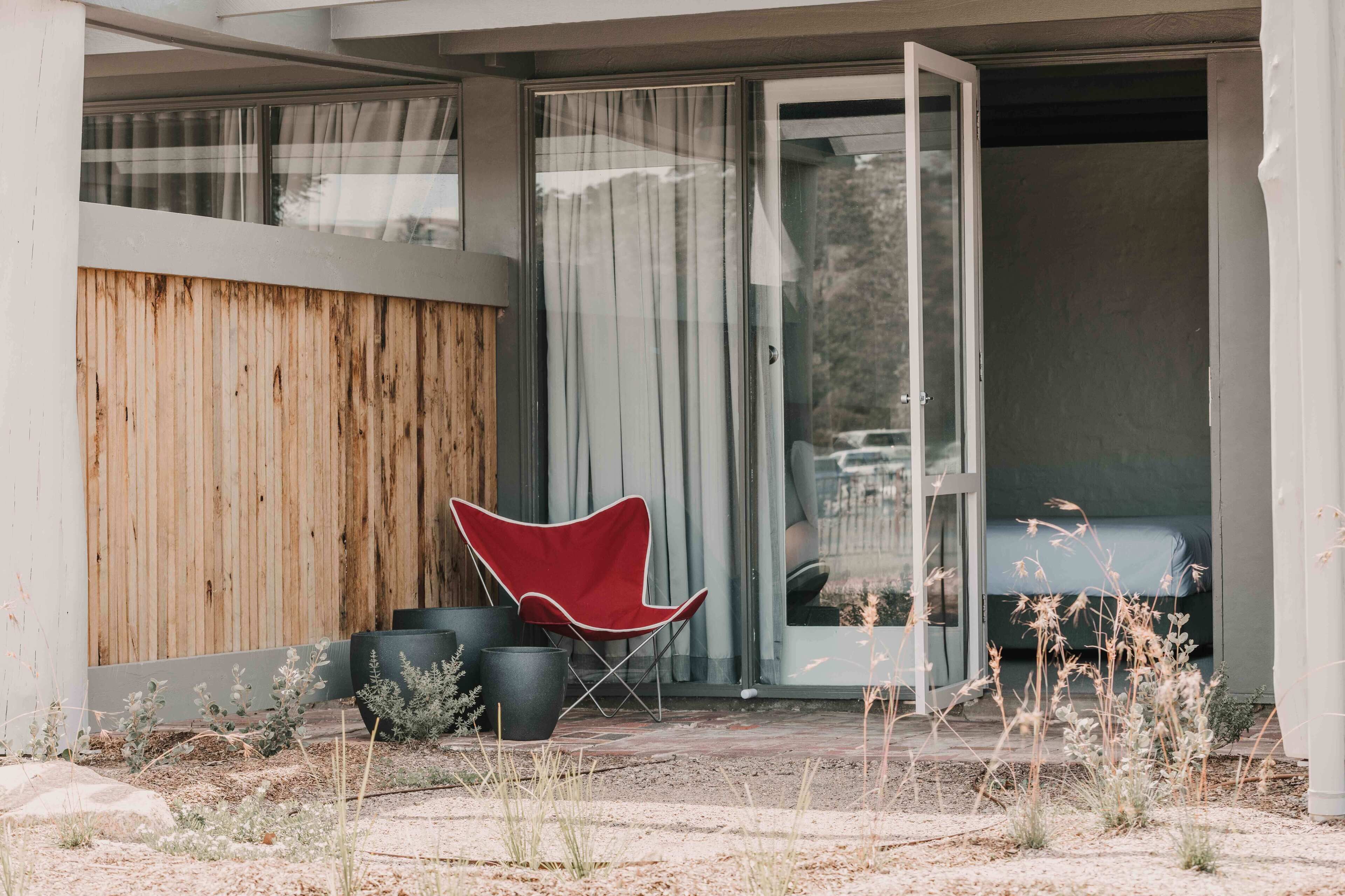 A modern building with a wooden exterior wall, a red chair, and potted plants in the foreground.