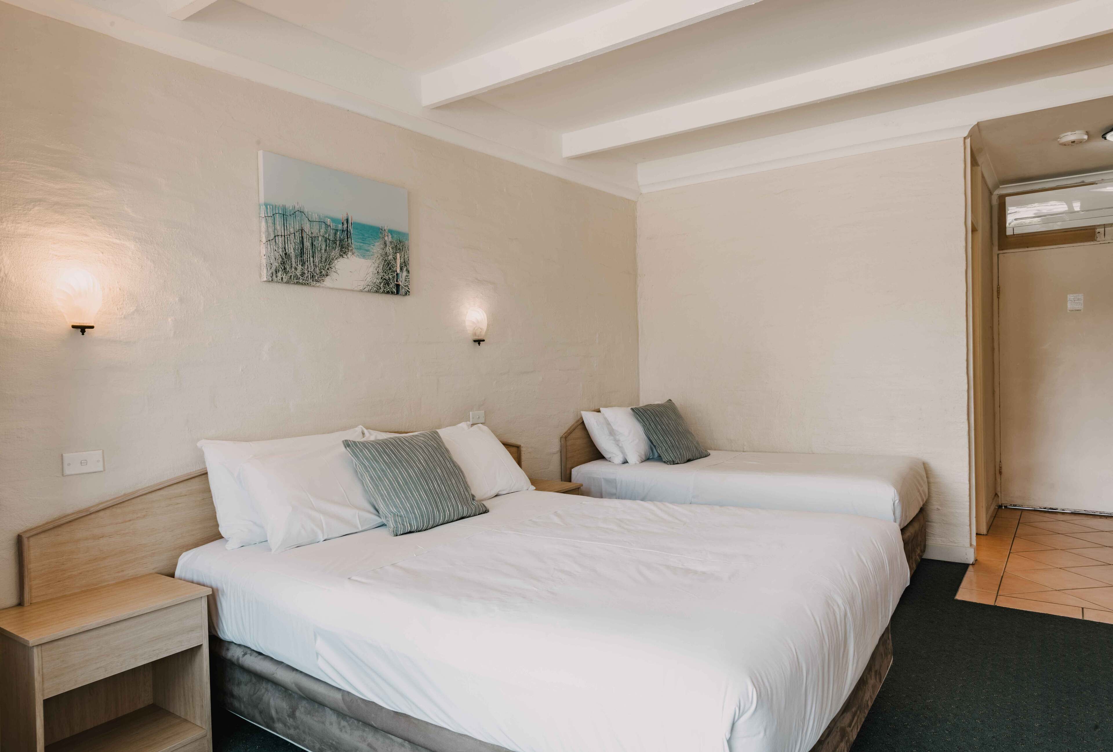 A hotel room with two beds, a nightstand, a painting on the wall, and a door to the right.