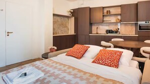 Een moderne hotelkamer met een bed, een zithoekje, een kitchenette en een deur.
