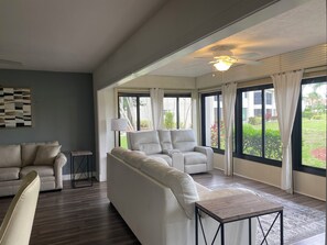 Ein geräumiges Wohnzimmer mit großem Fenster, Deckenventilator und einem modernen Sofa.