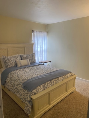 A bedroom with a bed, a nightstand, a window with curtains, and a carpeted floor. - Peaceful Condo -Golf Course & Sunset Views -Min stay required (Fort myers)