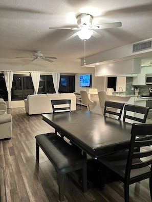 A modern living room with a dining area, a ceiling fan, and a flat-screen TV mounted on the wall. - Peaceful Condo -Golf Course & Sunset Views -Min stay required (Fort myers)