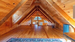 Ein Schlafzimmer im Dachgeschoss mit Holzbalken, Holzboden und Blick durch die geöffnete Tür.