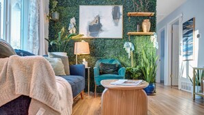 Een moderne woonkamer met een groene wand, een blauwe bank, een blauwgroene fauteuil en een houten salontafel.