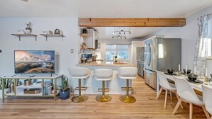 Een moderne keuken met een centraal kookeiland, witte barstoelen en een eethoek met een lange tafel voor zes personen.